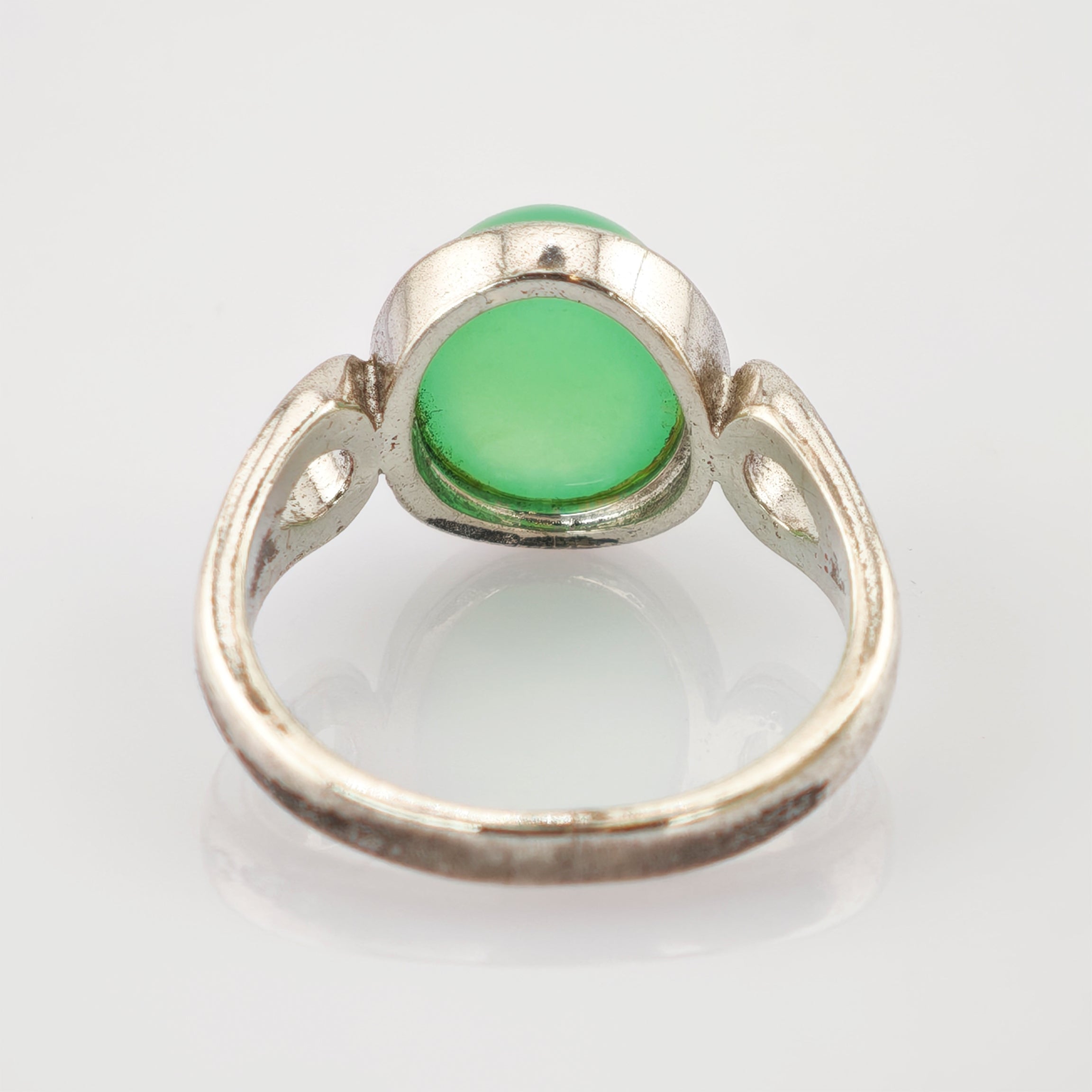 Antiker Silberring mit rundem grünem Edelstein auf einer reflektierenden weißen Oberfläche.