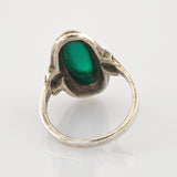 Antiksilberring mit ovalem grünem Edelstein auf reflektierender weißer Oberfläche.