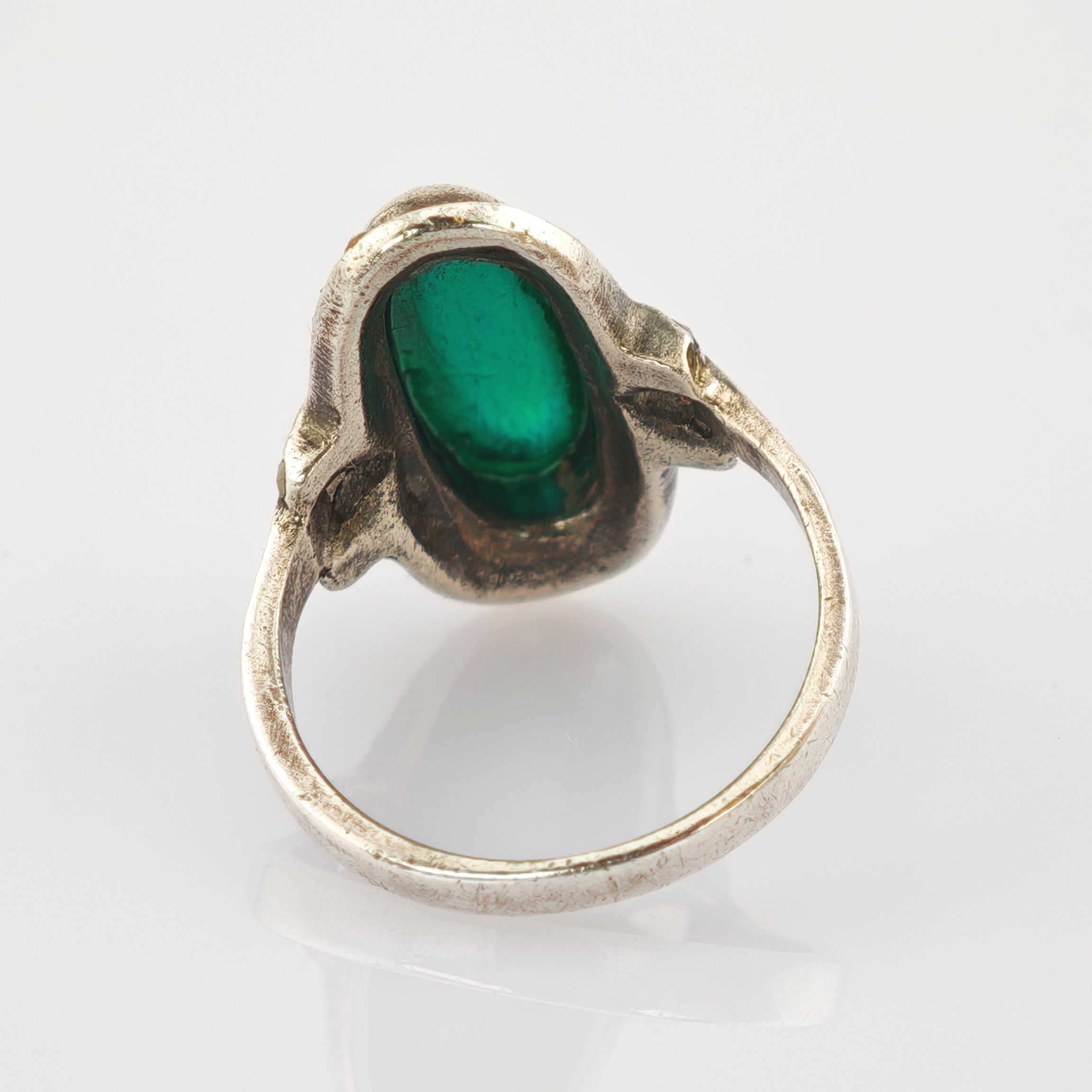 Antiksilberring mit ovalem grünem Edelstein auf reflektierender weißer Oberfläche.