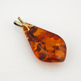 Polierter, tropfenförmiger Bernsteinanhänger mit sichtbaren floralen Einschlüssen und goldfarbener Metallöse.