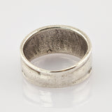 Breiter Metallschlichter Ring mit matter Oberfläche und leichten Gebrauchsspuren auf weiß reflektierendem Hintergrund.