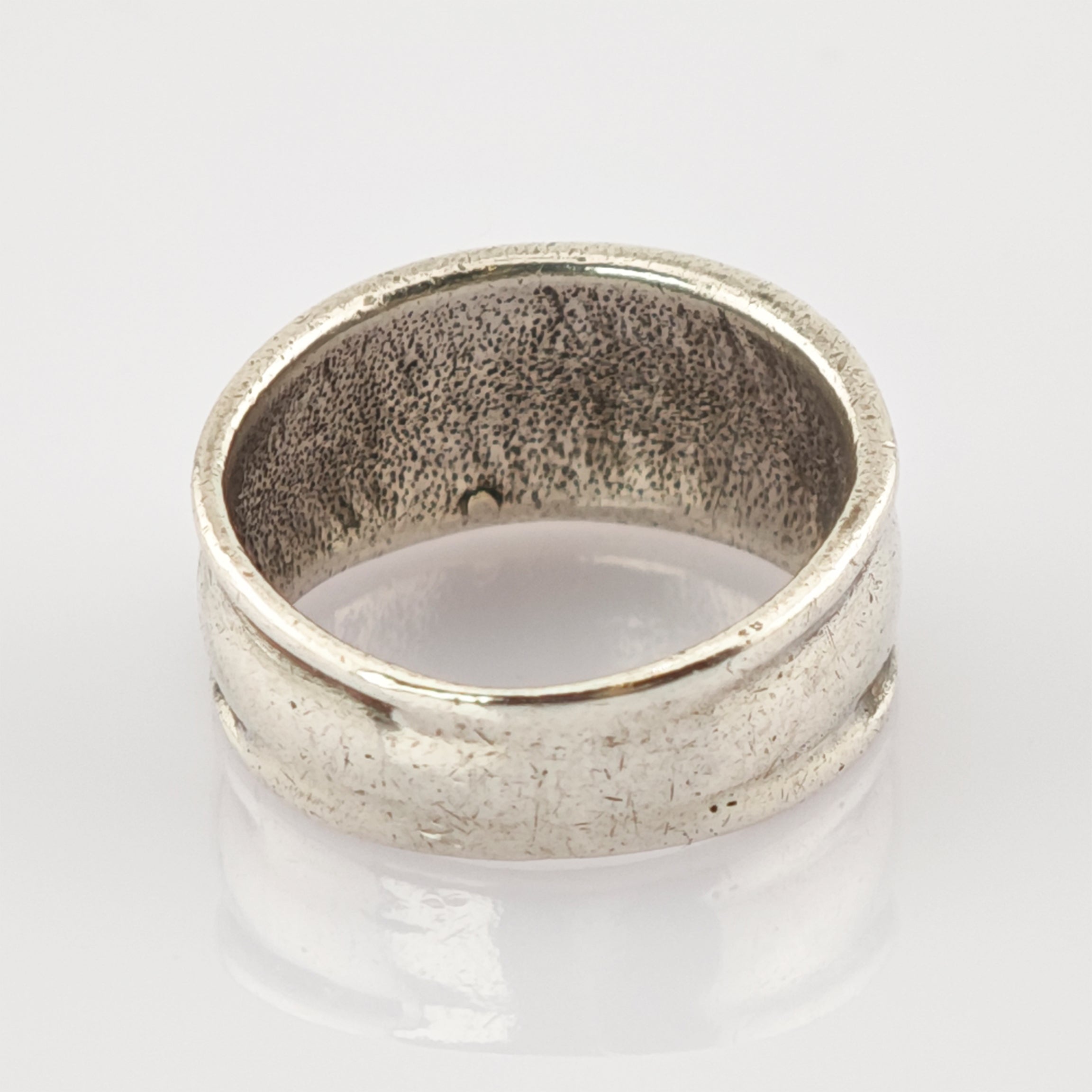 Breiter Metallschlichter Ring mit matter Oberfläche und leichten Gebrauchsspuren auf weiß reflektierendem Hintergrund.