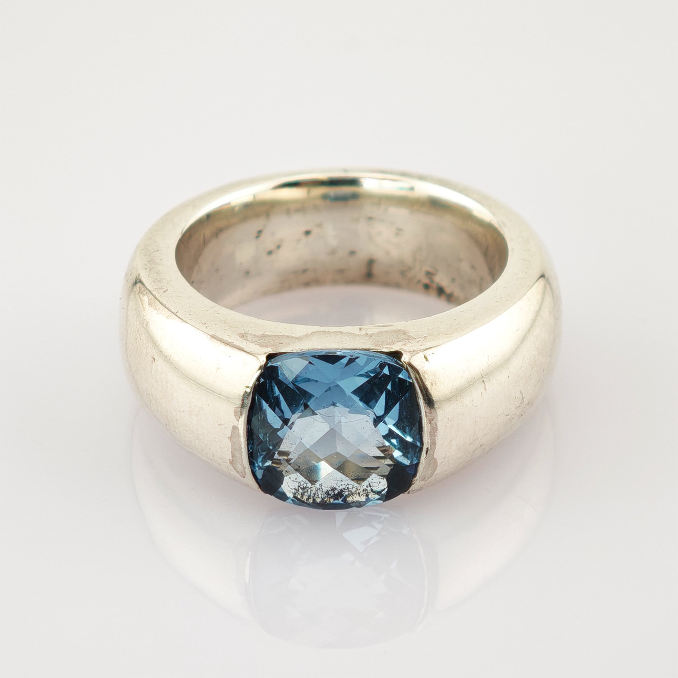 Breiter silberner Ring mit kissenförmigem, facettiertem blauen Edelstein und polierter Oberfläche