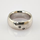 Breiter Silberring mit drei kleinen klaren diagonal angeordneten Edelsteinen auf glänzender Oberfläche.