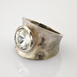 Breiter Silberring mit großem, rund facettiertem klarem Edelstein, sichtbaren Kratzern und Anlaufspuren.