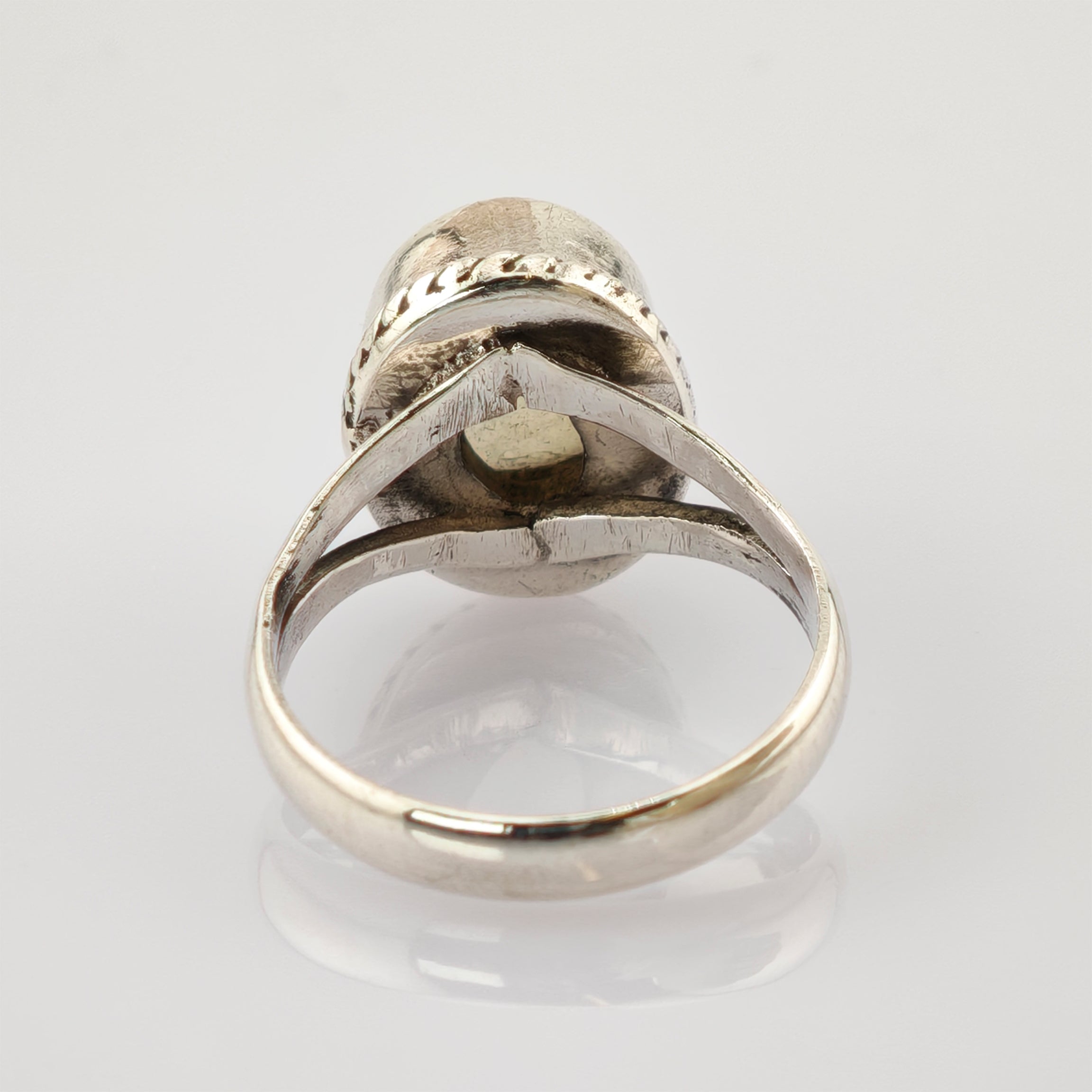 Detaillierter Silberring mit geteiltem Ringband auf reflektierender weißer Oberfläche.