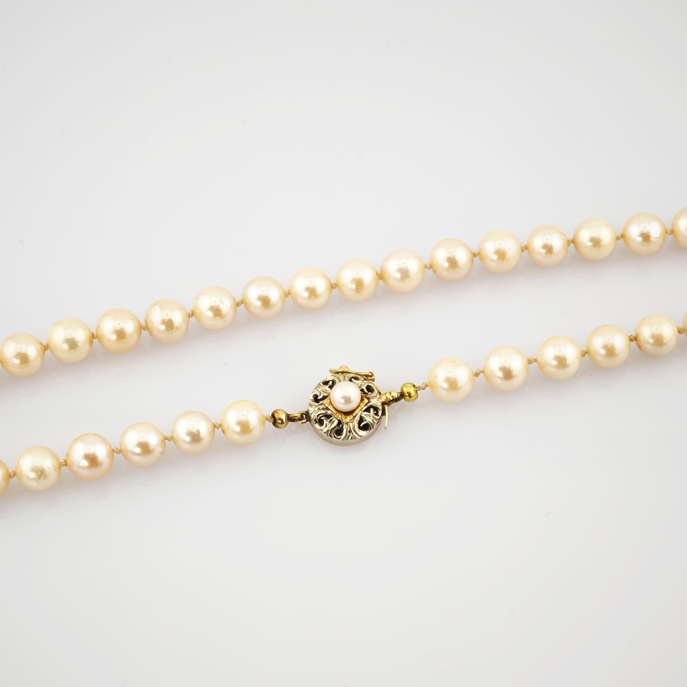 Edel wirkende Perlenkette mit cremefarbenen, kugelförmigen Perlen und dekorativem, rundem Goldverschluss mit kleiner Perle.