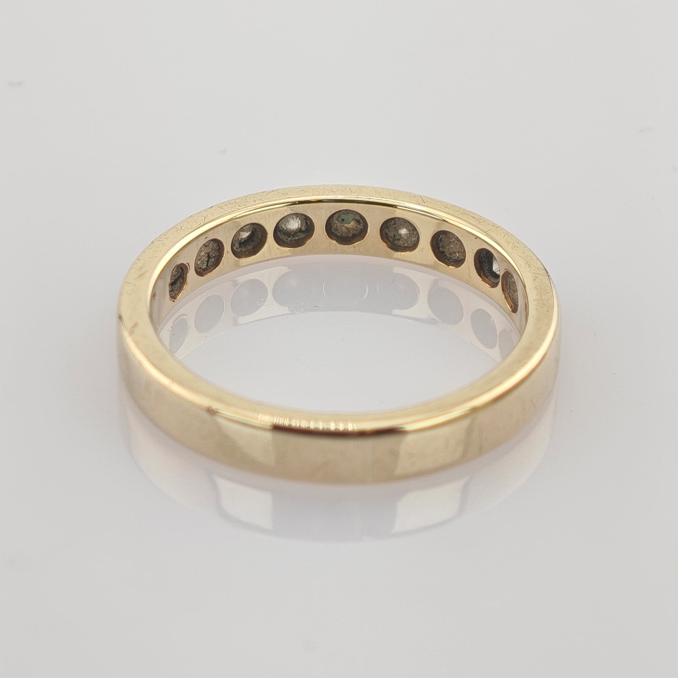 Einfacher goldfarbener Ring mit Gravur '10KT MEX 2H DE 14' auf der Innenseite, reflektierend auf heller Fläche.