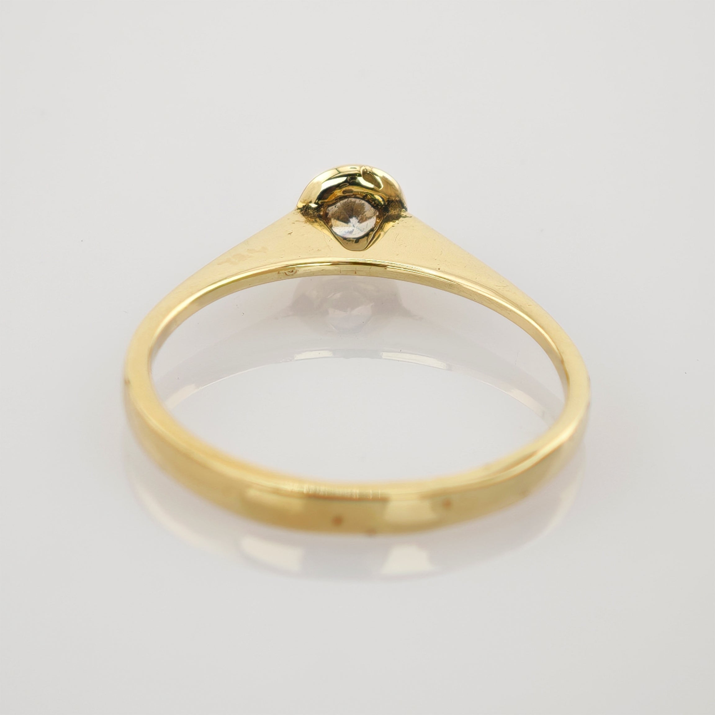 Eleganter Goldring mit kleinem Diamanten im minimalistischen Design auf hellgrauem Hintergrund.