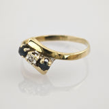 Goldring mit asymmetrischem Band und drei Steinen, zwei dunkelblau und einem klaren, auf weißem Eleganter Goldring mit gebogenem Steinbesatz aus zwei dunkelblauen und einem weißen Edelstein.