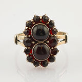 Eleganter Goldring mit zwei ovalen dunklen Steinen und kleineren facettierten dunkelroten Steinen in floraler Anordnung.