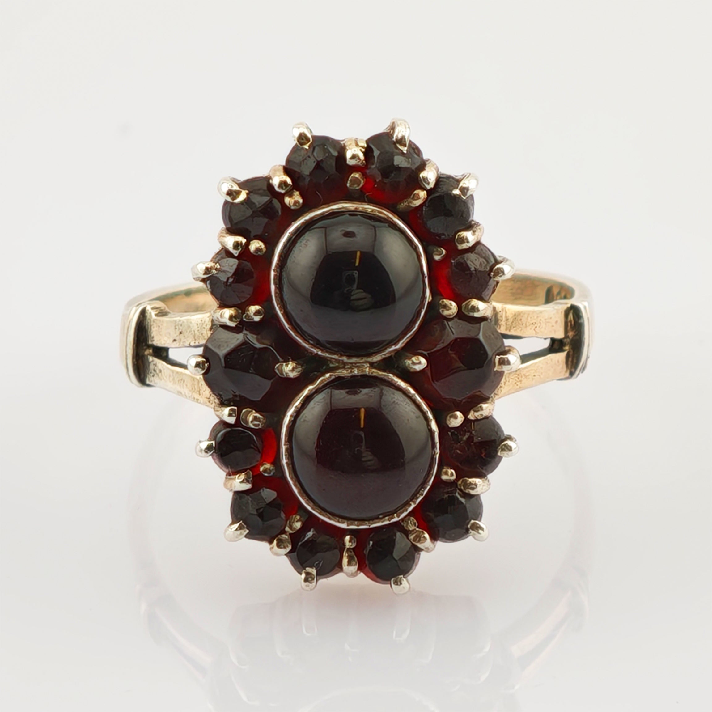 Eleganter Goldring mit zwei ovalen dunklen Steinen und kleineren facettierten dunkelroten Steinen in floraler Anordnung.