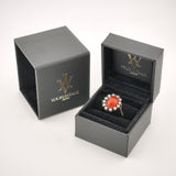 Eleganter goldener Ring mit ovalem rot-orangefarbenem Edelstein und klaren Steinen in schwarzer Samtschachtel.