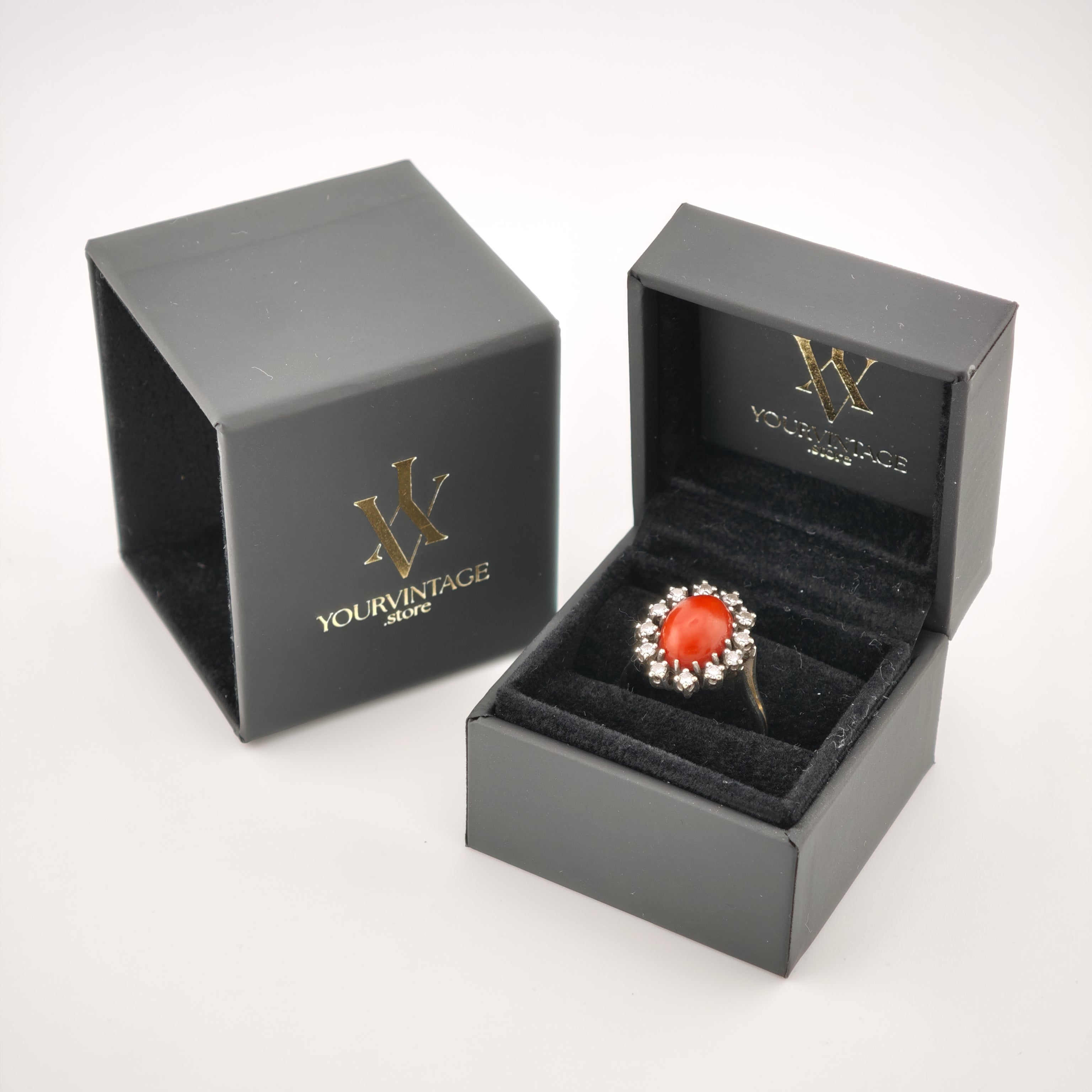 Eleganter goldener Ring mit ovalem rot-orangefarbenem Edelstein und klaren Steinen in schwarzer Samtschachtel.