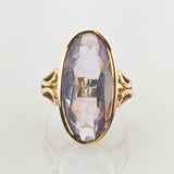 Eleganter Goldring mit großem, vertikal ovalem violettem facettiertem Edelstein und kunstvollen Metallverzierungen