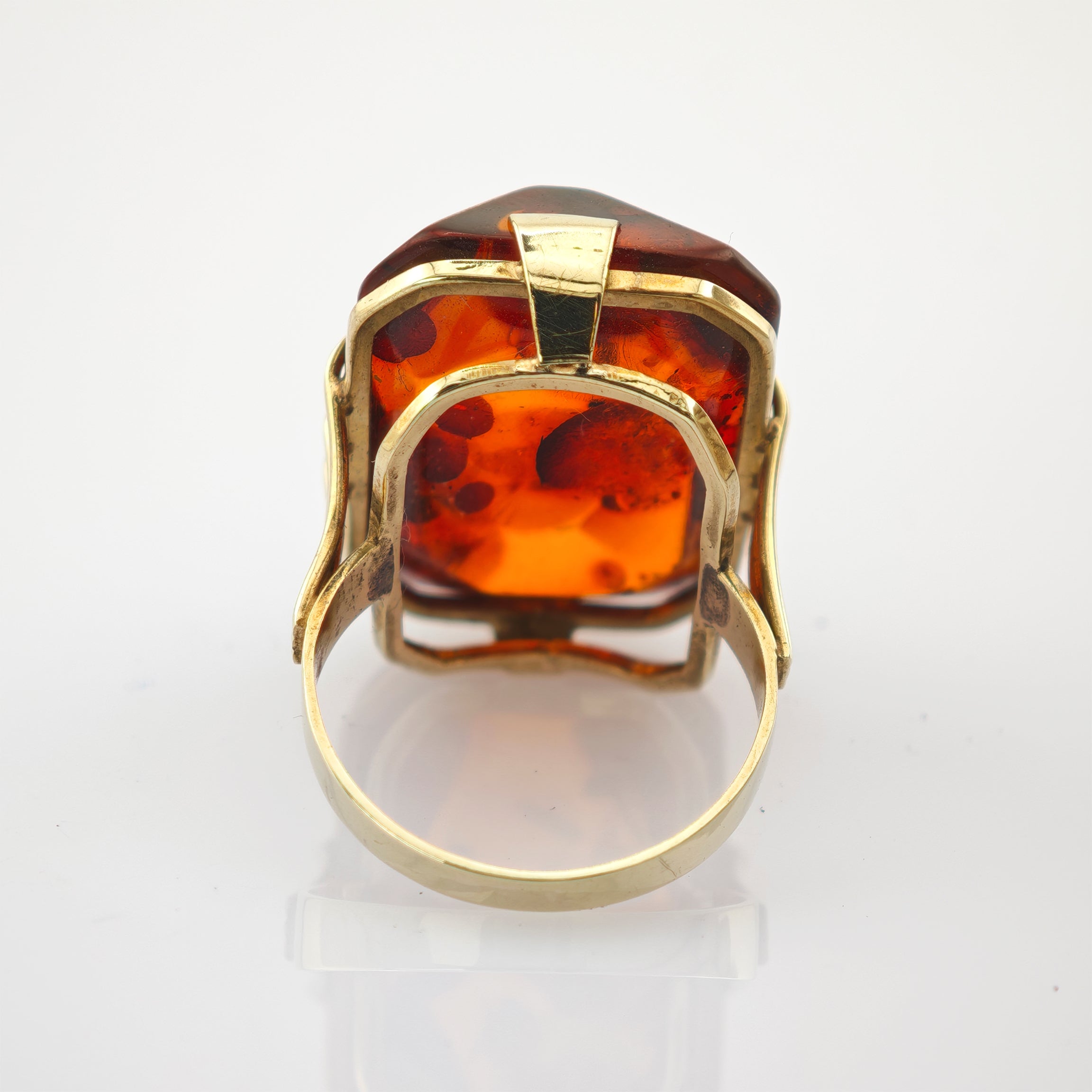 Eleganter Ring mit rechteckigem Bernstein und Goldfassung auf weiß reflektierender Oberfläche.