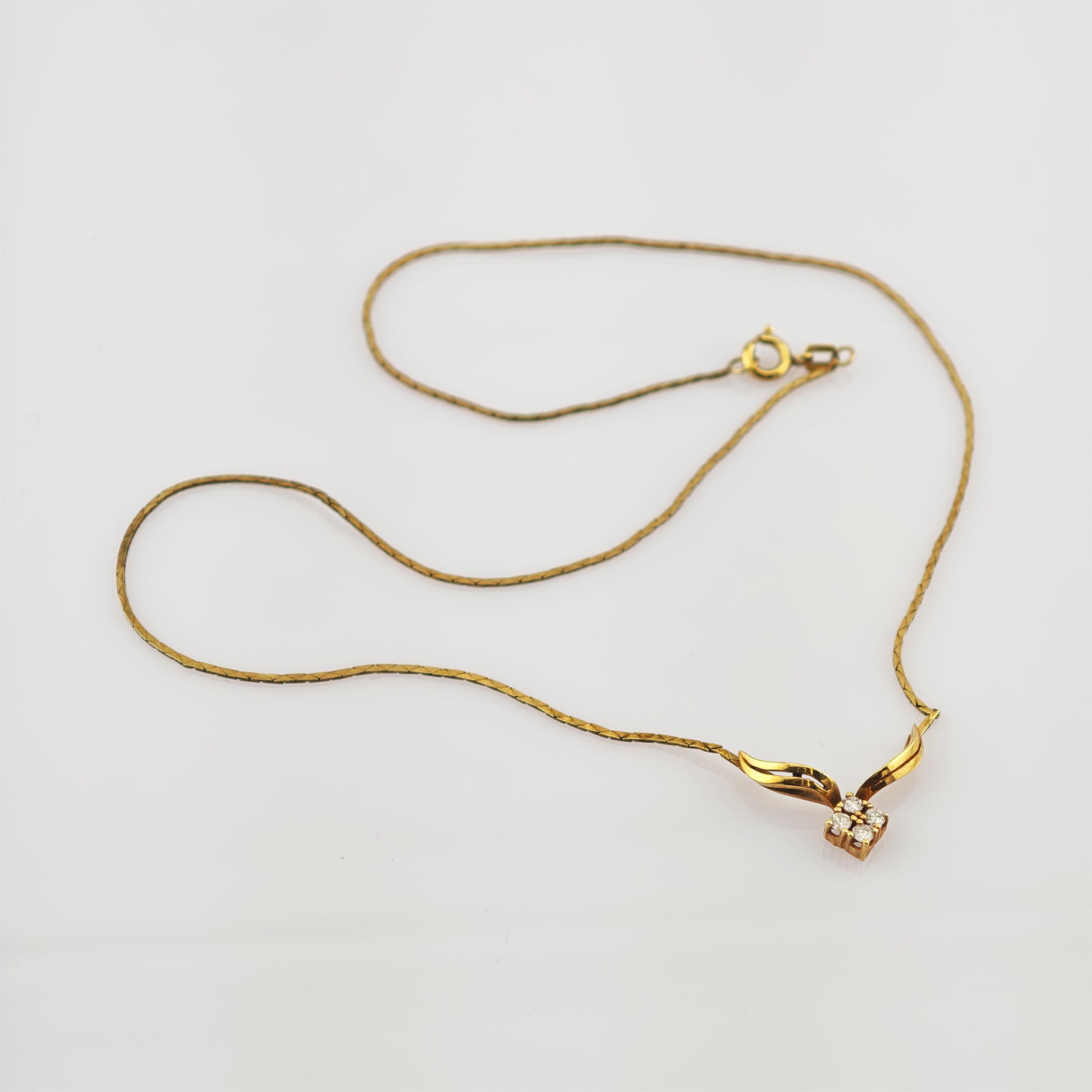 Feine Goldkette mit Anhänger aus flügelförmigen Goldelementen und Diamanten auf weißem Hintergrund.