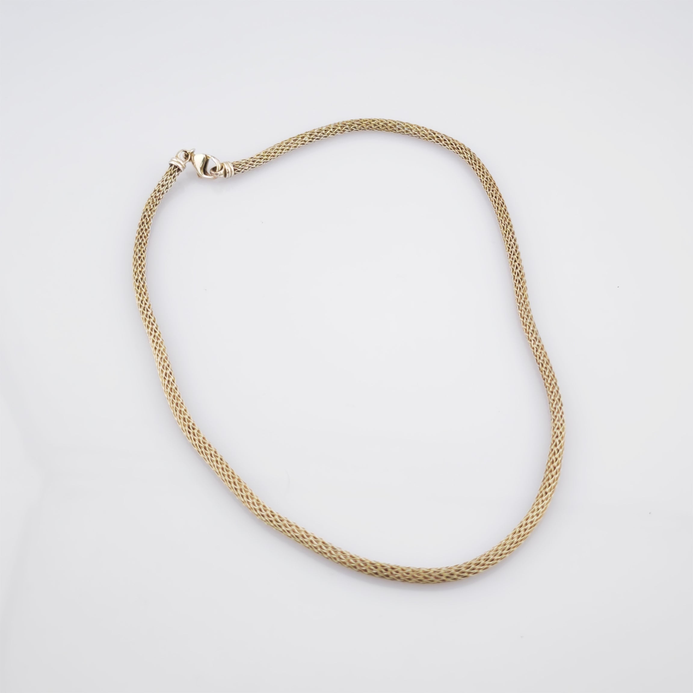 Feine Goldkette mit gewebter Mesh-Textur und Karabinerverschluss auf weißem Hintergrund.