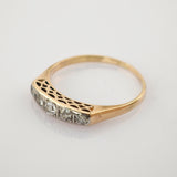 Feiner Goldring mit flacher Oberseite und fünf klaren Steinen in Reihe neben filigranem ausgeschnittenem Muster.