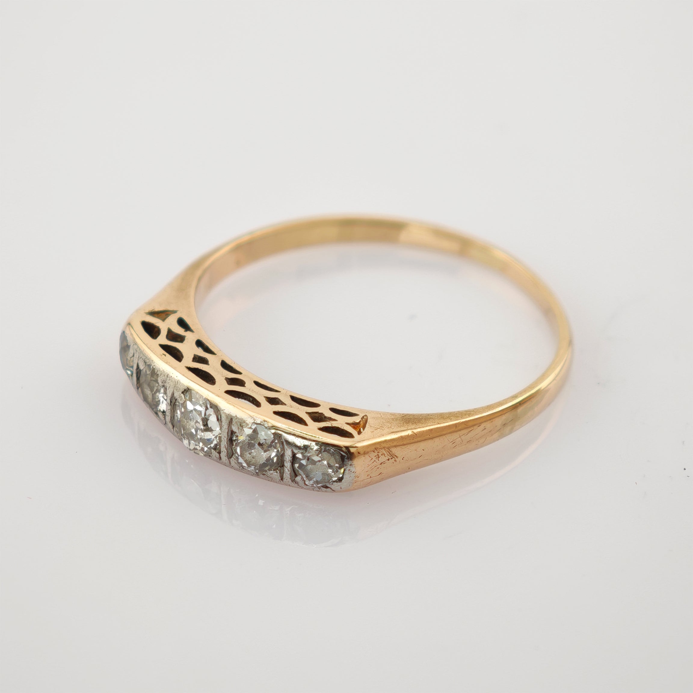 Feiner Goldring mit flacher Oberseite und fünf klaren Steinen in Reihe neben filigranem ausgeschnittenem Muster.
