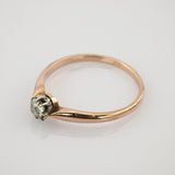 Feiner Goldring mit kleinem Diamant in Silberfassung auf reflektierender weißer Oberfläche