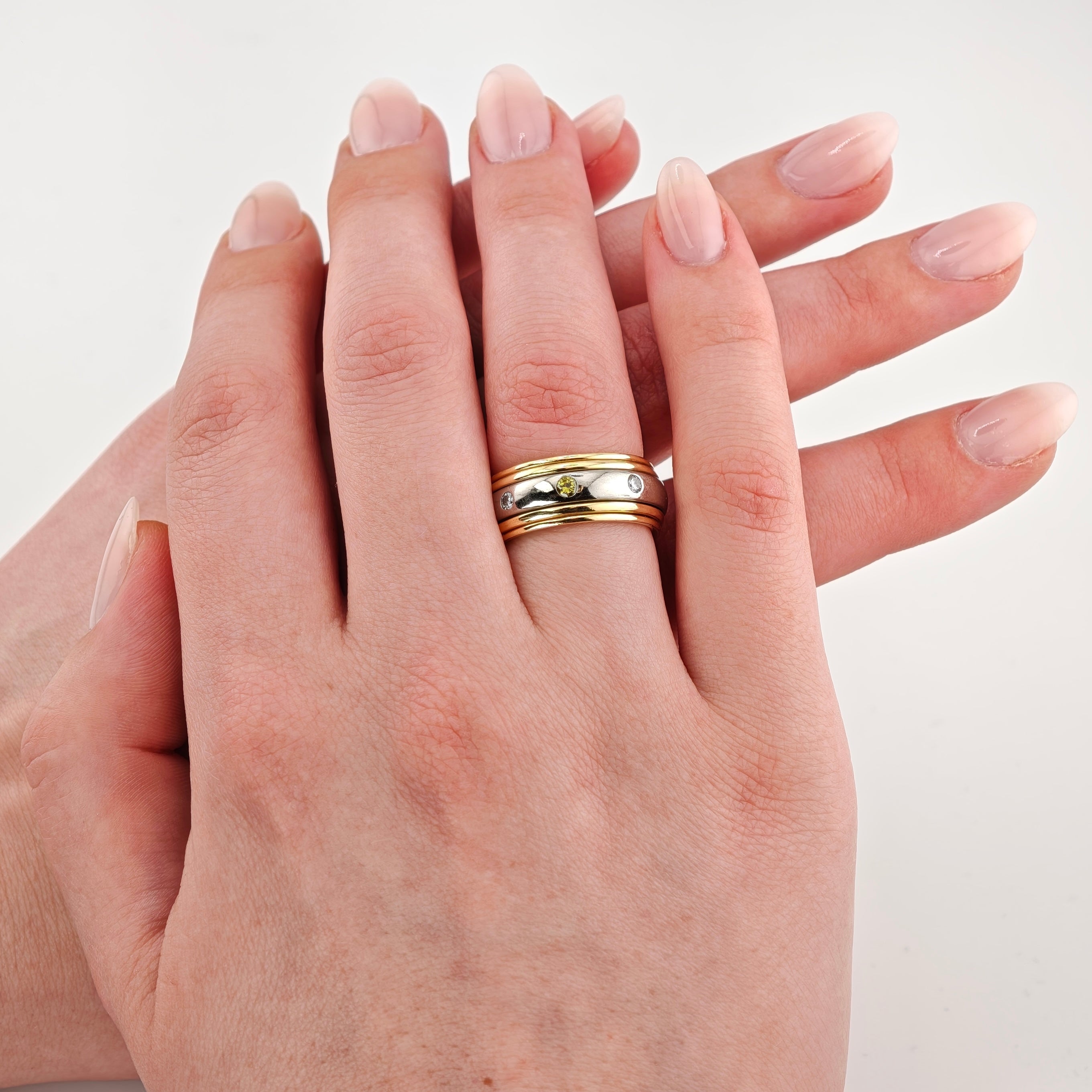 Zwei gepflegte Hände, eine trägt einen gold-silbernen Ring mit gelbem Edelstein und klaren Steinen.