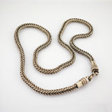 Geschwungene geflochtene Metallkette in gold-bronze auf weißem Hintergrund.