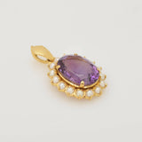Goldanhänger mit großem ovalen, violetten, facettierten Edelstein, umgeben von weißen Perlen.