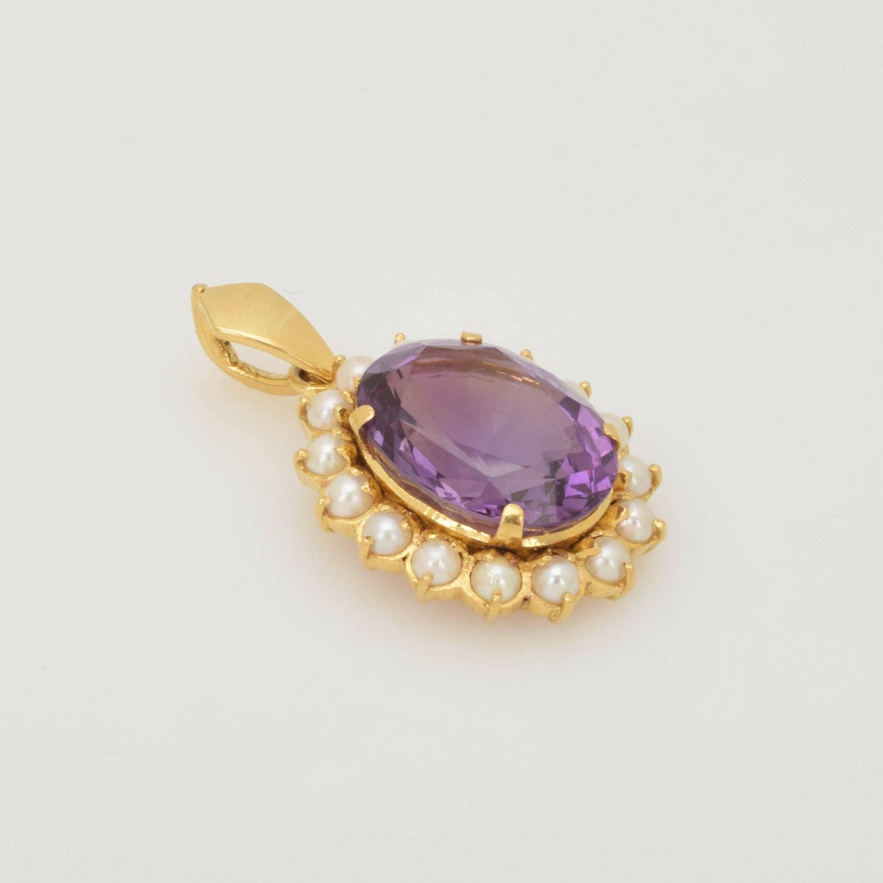 Goldanhänger mit großem ovalen, violetten, facettierten Edelstein, umgeben von weißen Perlen.