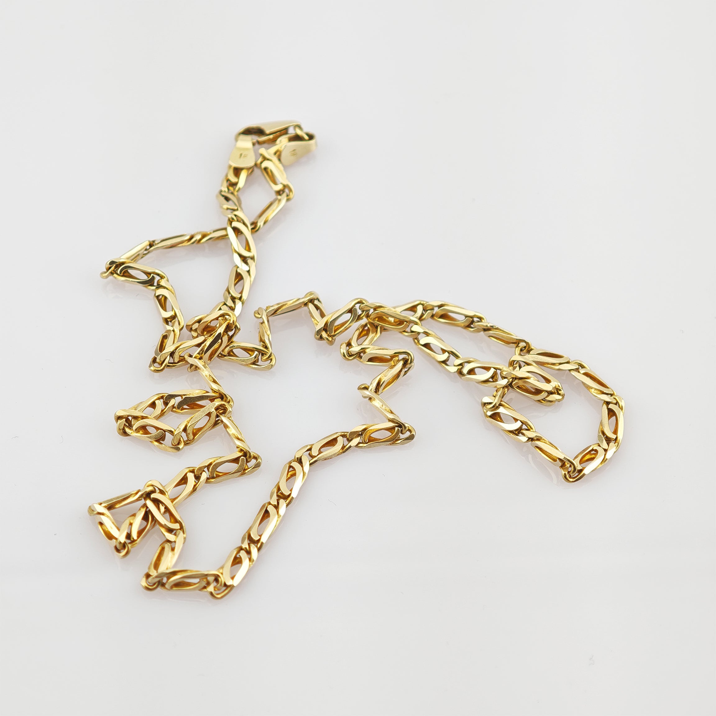 Goldene Halskette mit filigranen ovalen und verdrehten Gliedern auf weißem Hintergrund.