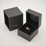Goldener Knotenring in offenem schwarzen Samt-Ringkästchen mit goldfarbenem Logo.