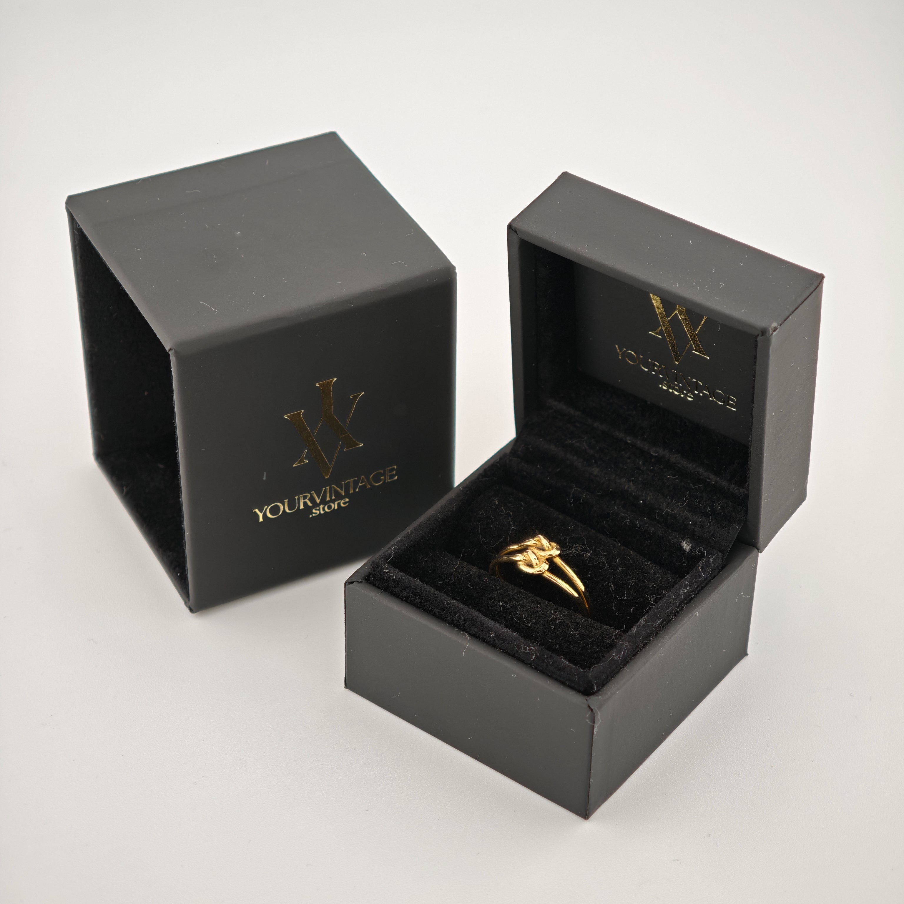 Goldener Knotenring in offenem schwarzen Samt-Ringkästchen mit goldfarbenem Logo.