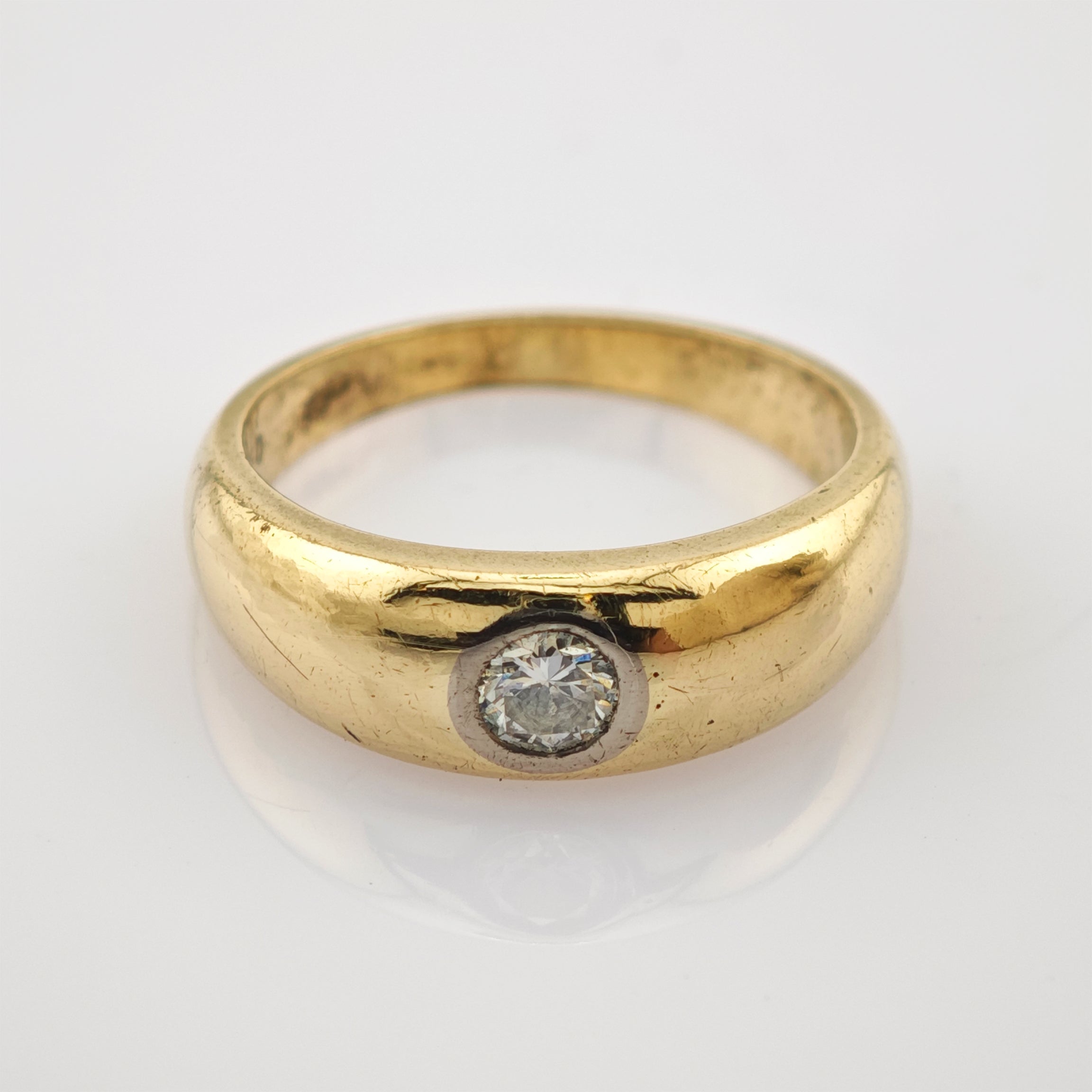 Goldener Ring mit rundem Band und Einzel-Diamanten auf reflektierender weißer Oberfläche