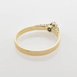 Goldener Ring mit filigranem Design und kleinem Zentrumstein auf reflektierender Oberfläche.