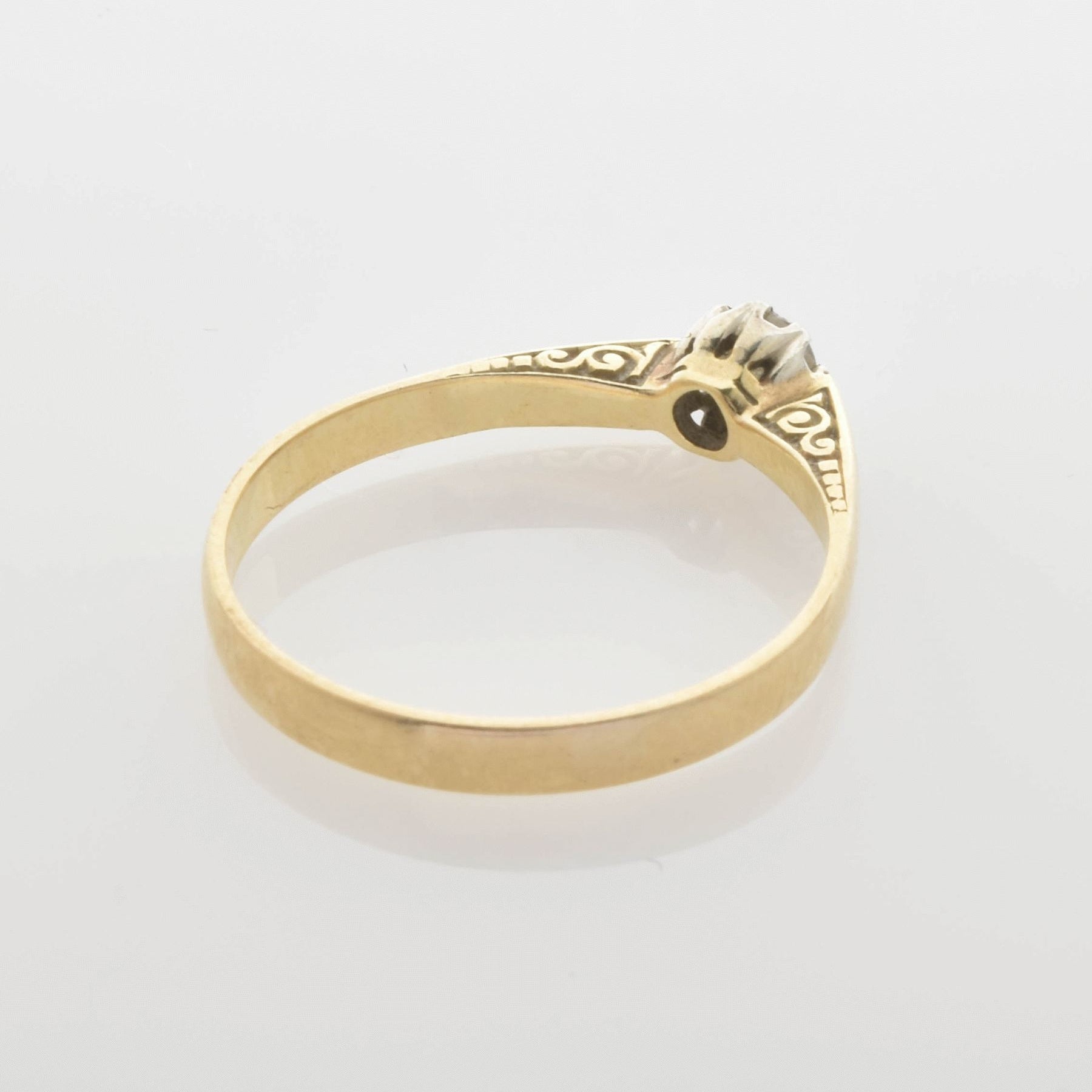 Goldener Ring mit filigranem Design und kleinem Zentrumstein auf reflektierender Oberfläche.