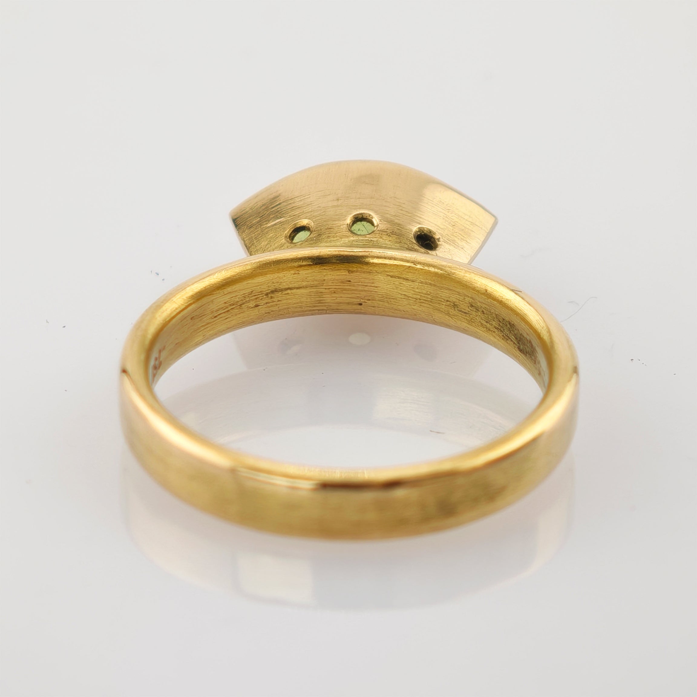 Goldener Ring mit halbkreisförmiger Platte und drei runden Inlays auf weißer Oberfläche.