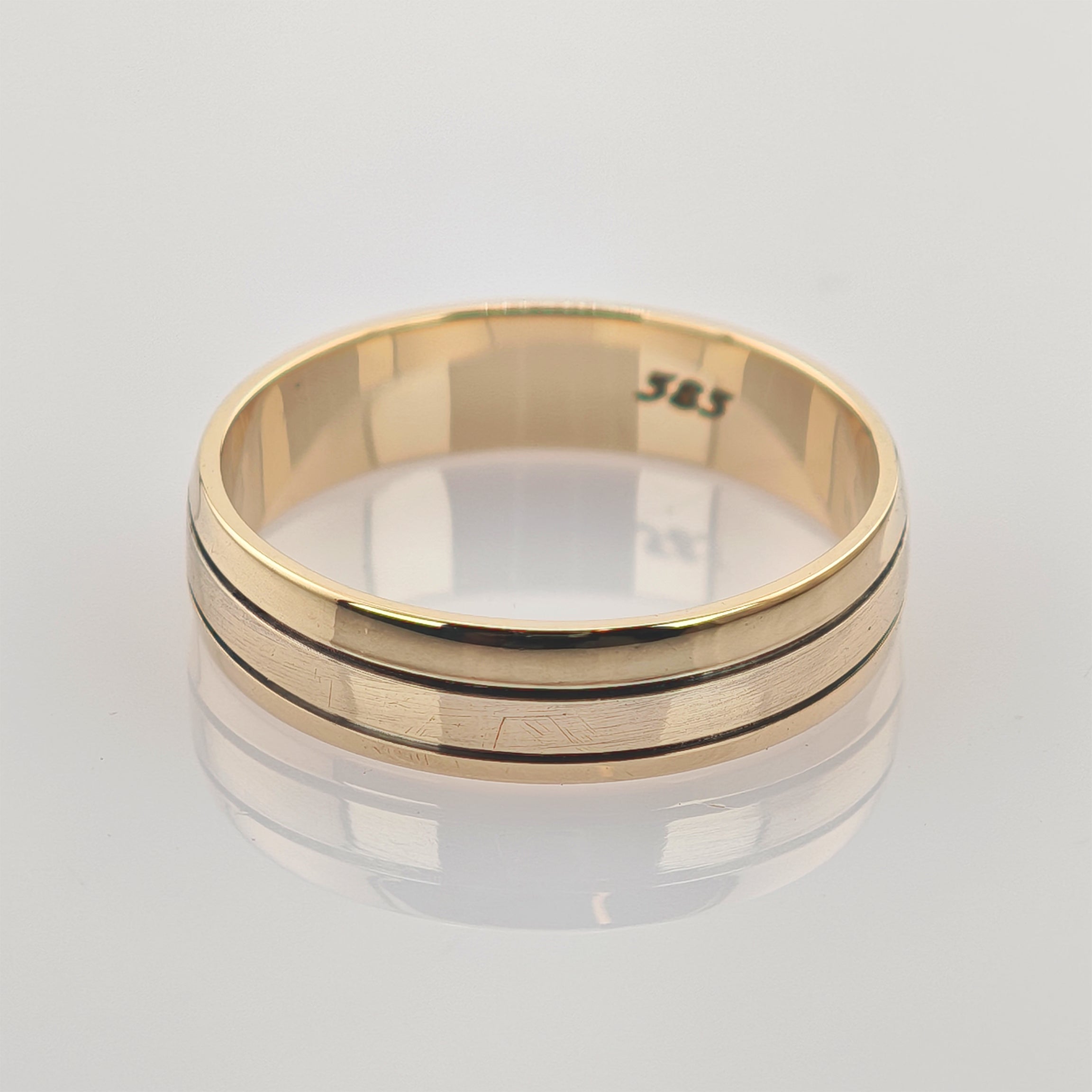 Goldener Ring mit mittlerer Rille auf glatter Oberfläche mit Spiegelung.
