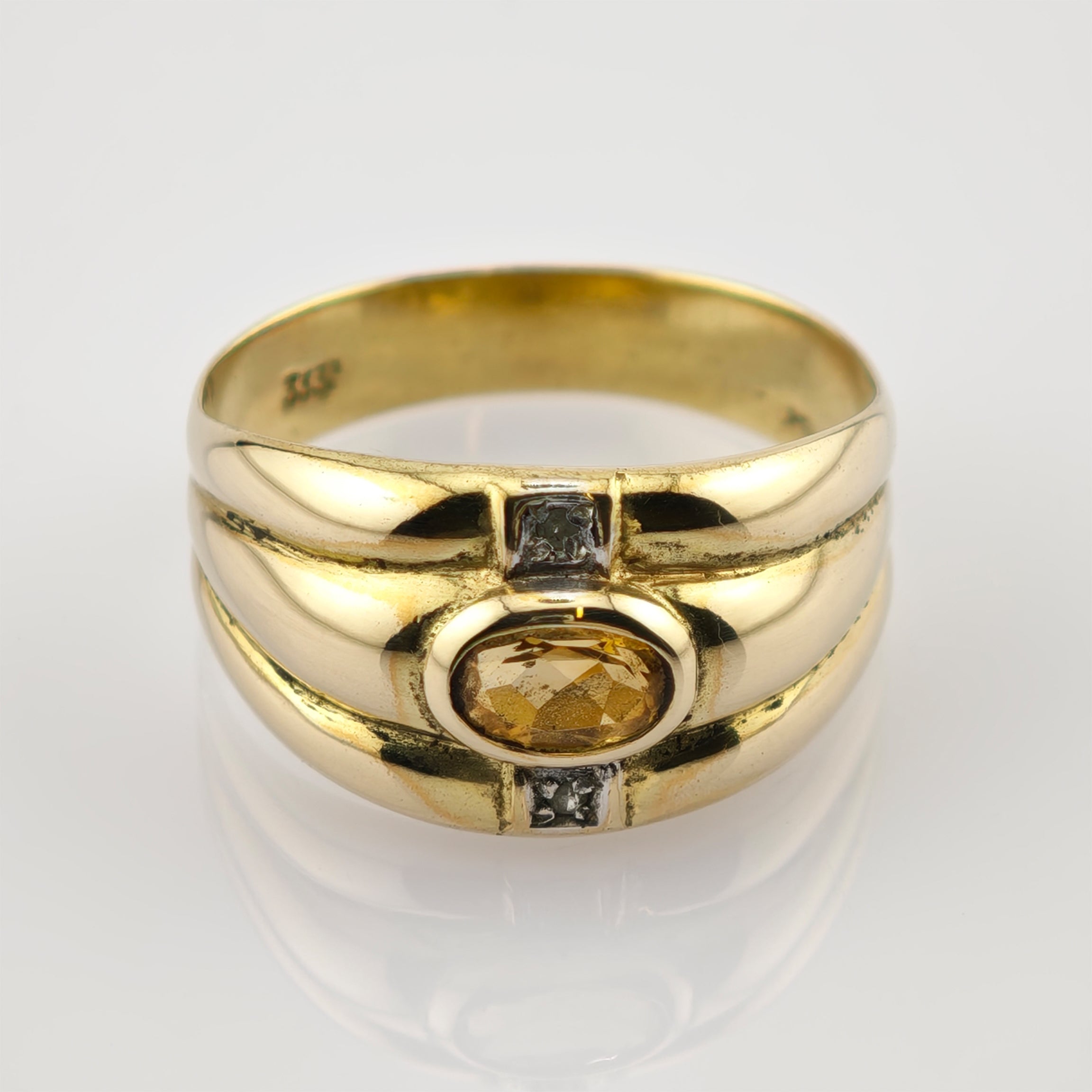 Goldener Ring mit ovalem gelbem Edelstein und zwei klaren Steinen auf weißem Hintergrund.