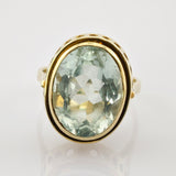 Goldener Ring mit großem ovalem facettiertem hellgrünem Schmuckstein und dekorativen Rundausschnitten