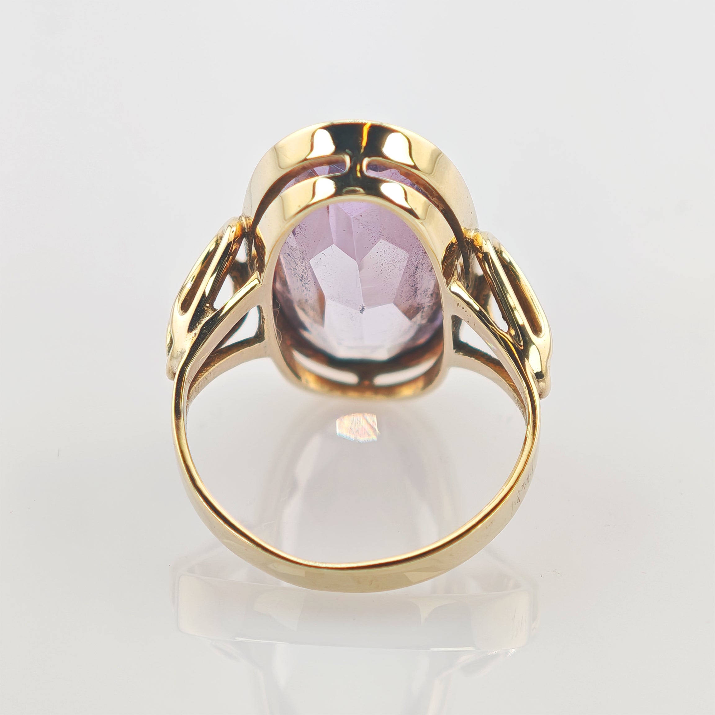 Goldener Ring mit ovalem lila Edelstein und filigraner Goldfassung auf reflektierendem Untergrund