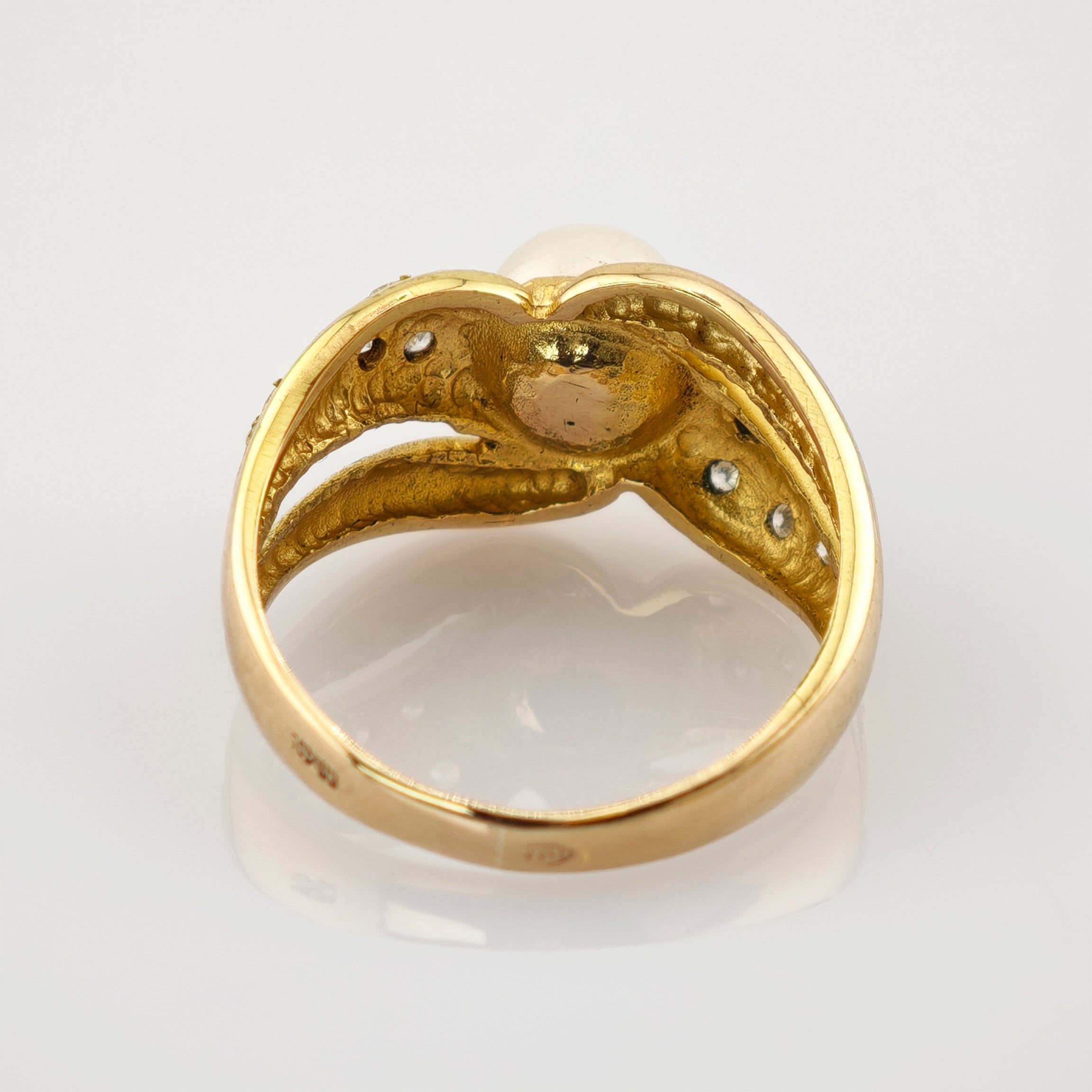 Nahaufnahme eines goldenen Rings mit Perle und detaillierter Innenstruktur, die feine Handwerkskunst zeigt