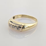 Goldener Ring mit poliertem Band und drei kleinen Diamanten in quadratischen Fassungen auf weißer reflektierender Oberfläche.