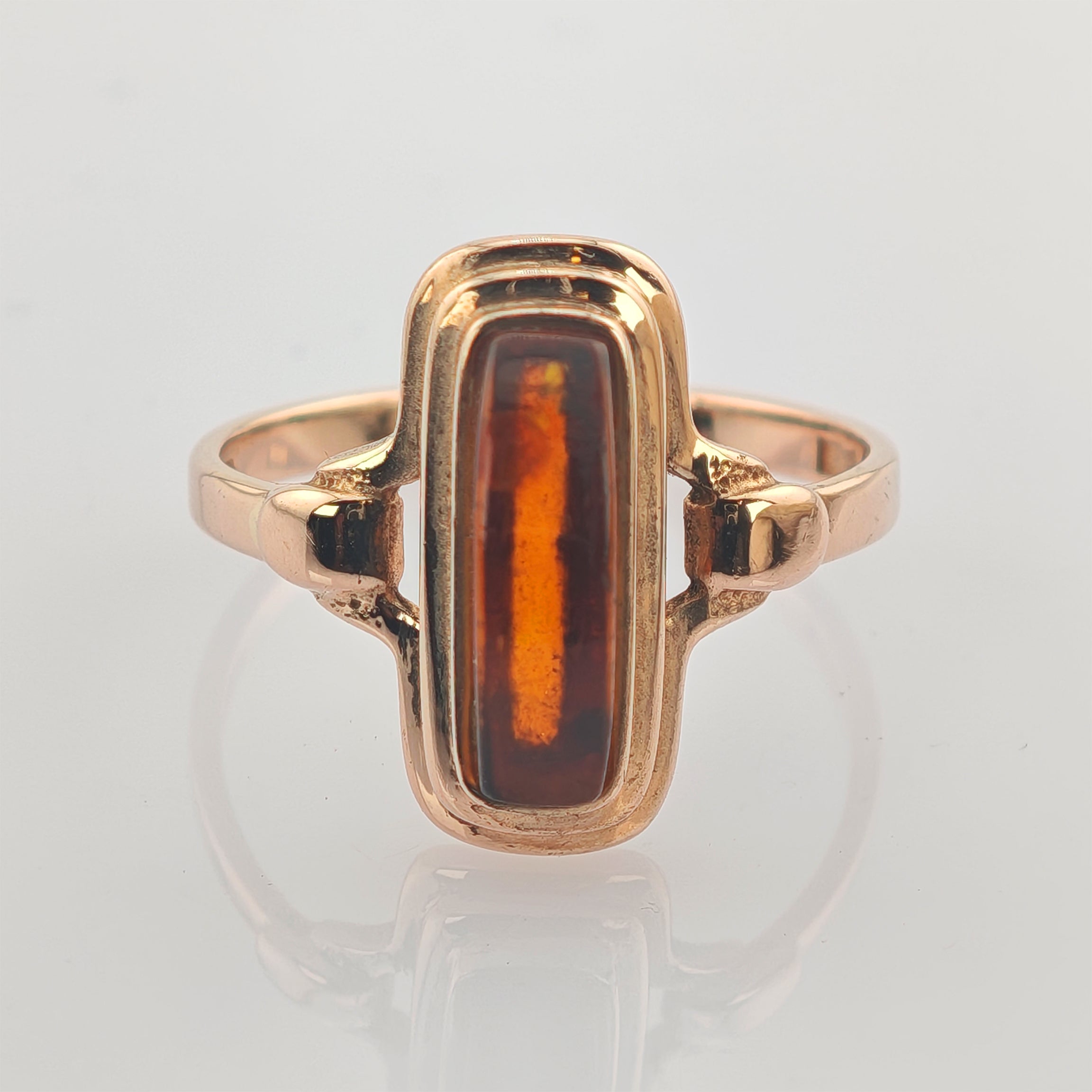 Goldener Ring mit rechteckigem, senkrecht eingesetztem Bernsteinelement auf hellgrauem Hintergrund