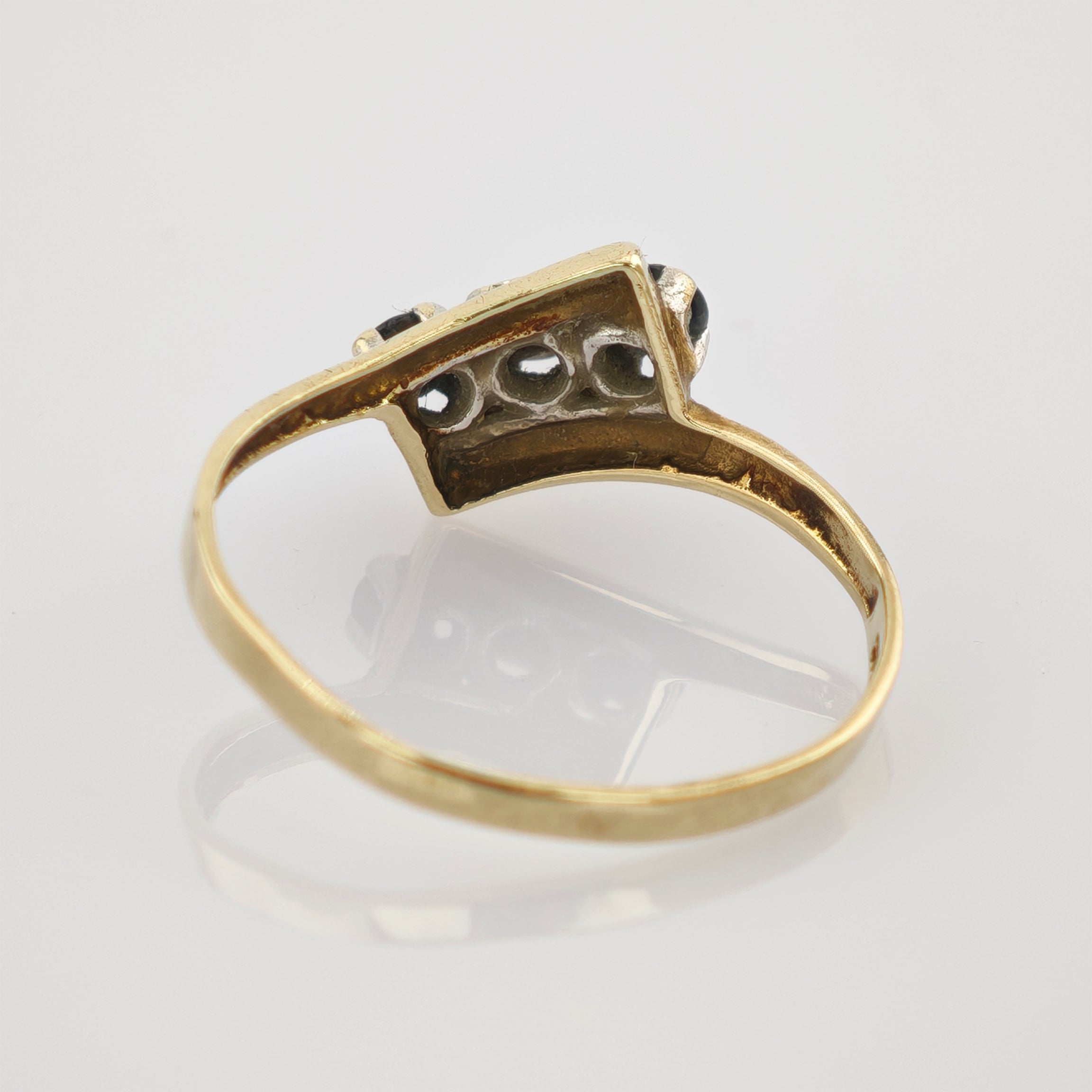 Goldener Ring mit sichtbarem Innenring auf spiegelnder Oberfläche im Goldener Ring mit rechteckigem Kopf und schwarzen Steinen auf weißem Untergrund