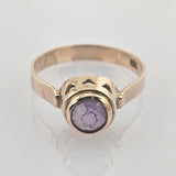Goldener Ring mit rundem lila Stein und zarter Fassung, zeigt feine Struktur und Vintage-Charakter.