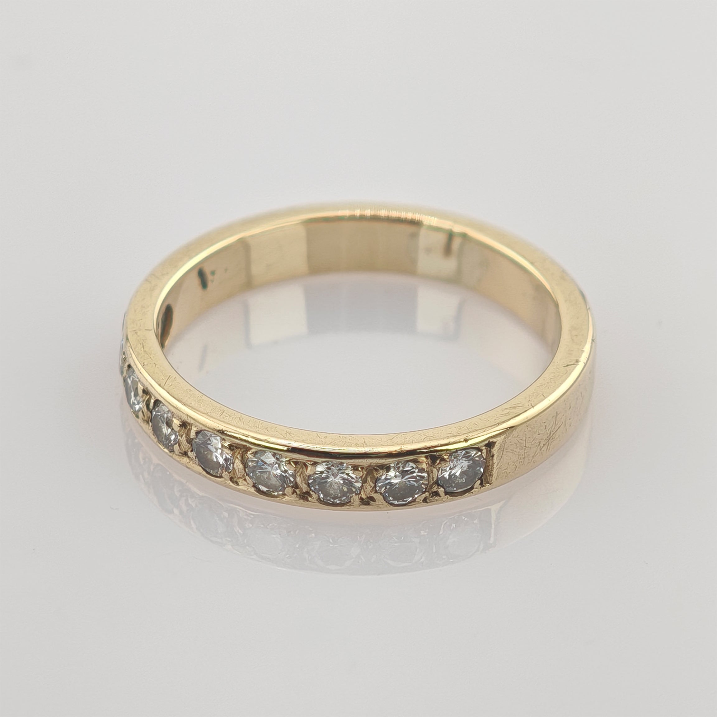 Goldener Ring mit sieben runden klaren Steinen auf reflektierendem weißen Hintergrund
