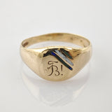 Goldener Siegelring mit stilisiertem Buchstaben B, verziert mit blauen und silbernen Details auf weißem Hintergrund.