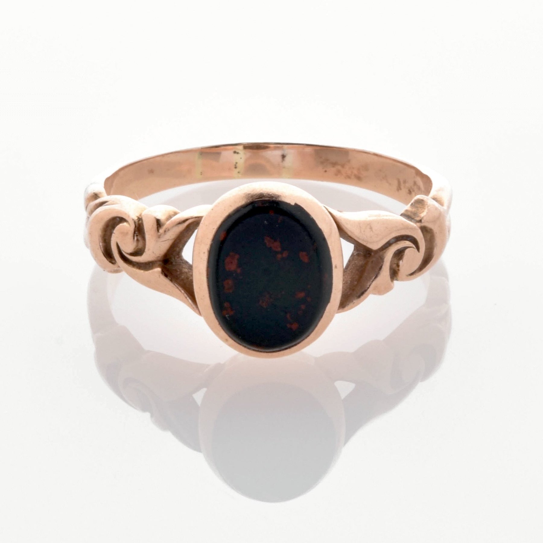 Goldener Vintage-Ring mit ovalem dunklem Stein und roten Einsprengseln, verziert mit Ornamenten, auf weißem Hintergrund.