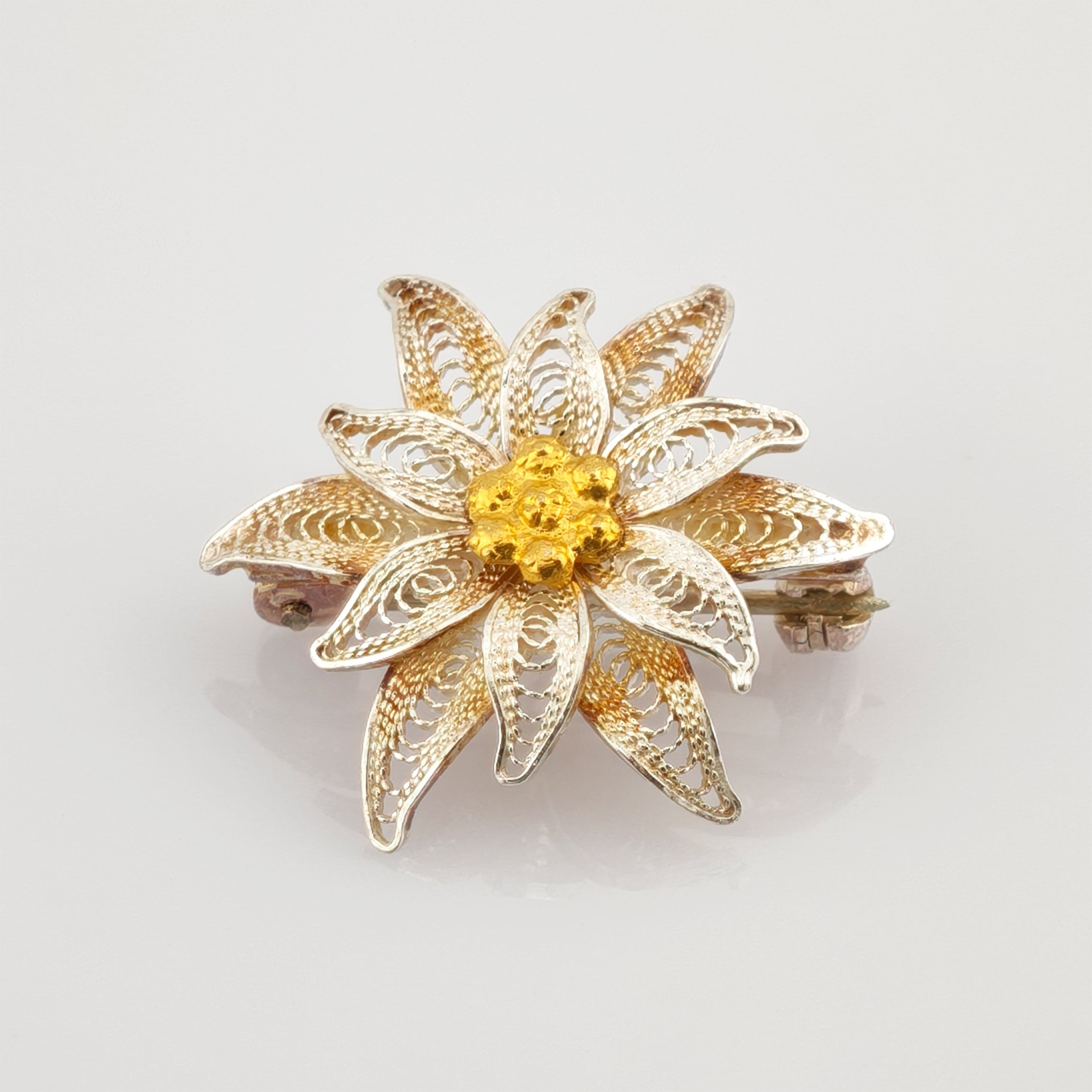 Goldfarbene Brosche in Form einer achtblättrigen Blume mit Netzmuster und strukturiertem Zentrum im Vintage-Stil.