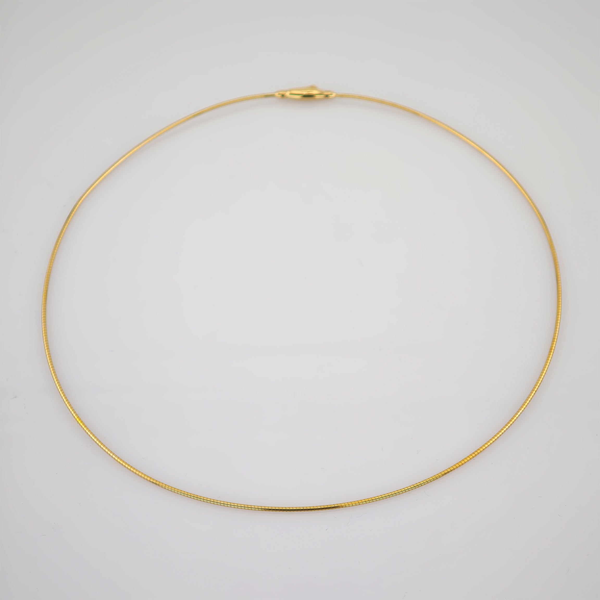 Zarte goldfarbene Halskette mit feiner Kettengliederung und Karabinerverschluss auf grauem Hintergrund
